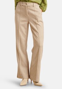 Pantaloni beige a gamba larga in tessuto morbido, con tasche frontali, chiusura con un bottone e dettagli di cuciture verticali.