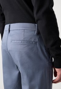 Pantalones azul claro hechos de una tela suave, con un bolsillo trasero que presenta un sutil logotipo de "Calvin Klein" y un corte entallado.