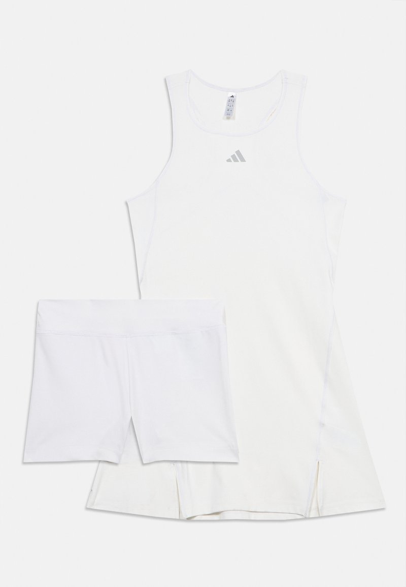 Λευκό αμάνικο αθλητικό φόρεμα με μικρό λογότυπο της Adidas και λευκά συμπιεστικά σόρτς που φοριούνται από κάτω.