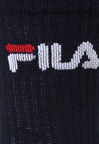 Jersey de punto en color navy con un destacado logo blanco de "FILA", con un acento rojo sobre la letra 'F'. Tejido texturizado con líneas verticales.