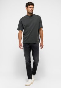 Camiseta de gran tamaño color gris oscuro con cuello redondo, combinada con jeans negros y zapatillas altas blancas. Tejido de algodón casual, corte relajado.