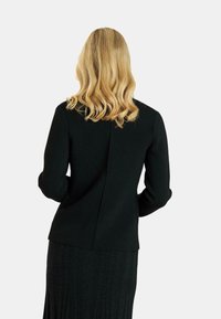 Blazer negro ajustado con una textura suave, mangas redondeadas y una costura vertical en la parte posterior, combinado con una falda acanalada a juego.
