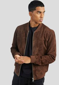 Veste aviateur en daim marron avec fermeture éclair à l'avant, poignets et ourlet côtelés. Présente une texture lisse et des coutures horizontales discrètes sur la poitrine.