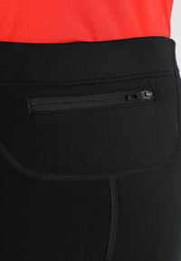Schwarze Sportleggings mit einer Reißverschlusstasche auf der Rückseite, glatter Textur, verst ärkten Nähten und einer enganliegenden Passform.