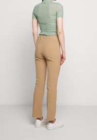 Beige fitted pants with a smooth texture, featuring a slight flare at the ankle. Paired with a green, textured mock neck top.