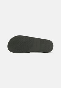 Suola di scarpa in gomma nera con un motivo di presa testurizzato, caratterizzata da un logo sottile e bordi lisci. Forma curva con punta arrotondata.