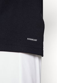 Svart atletisk tröja med en slät textur, med en vit "AEROREADY"-logotyp nära fållen. Designen betonar fukttransporterande prestanda.