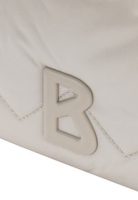 Vaaleanbeige laukku, joka on valmistettu sileästä nailonista ja jossa on teksturoitu chevron-kuviointi sekä korostava harmaa "B"-logo.