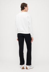 Witte oversized sweatshirt met geribbelde manchetten, gecombineerd met zwarte flared jeans. De outfit heeft een eenvoudig ontwerp en een zachte textuur.