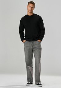 Sort langærmet skjorte, grå lige jeans, sort og hvidt sneakers, præsenteret mod en lys baggrund. Casual, minimalistisk design.