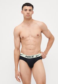 Sorte truser med en neongrønn Nike-linning, med en tett passform og glatt stoff. Sportsmerket logoen er tydelig vist.