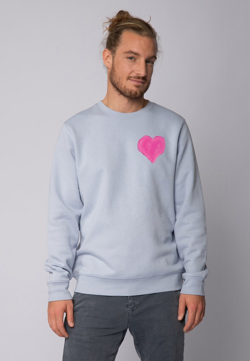 Sweatshirt bleu clair avec un design de cœur rose sur la poitrine gauche. Il a des manches longues et des poignets et un ourlet côtelés.