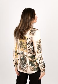 Satin long-sleeve blouse featuring a mix of leopard and graphic prints in beige, with black accents and a loose fit.
