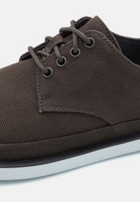 Scarpe in tela marrone con tomaia strutturata, punta rotonda, occhielli in metallo e suola in gomma bianca. I lacci sono dello stesso colore marrone.