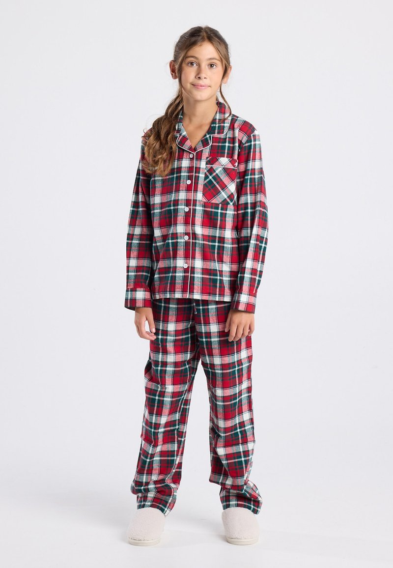 Rode en groene geruite pyjama set met een geknoopte shirt met een borstzakje en bijpassende broek, gemaakt van zachte stof. Witte, pluizige slippers.