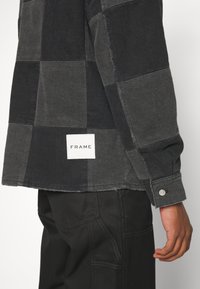Schwarzes und graues kariertes Hemd mit Knöpfen und ausgefranstem Saum. Verfügt über ein rechteckiges weißes "FRAME"-Label und silberne Knopfakzente.