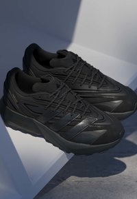 Čierne športové topánky s textúrovaným zvrškom, aerodynamickým dizajnom, gumovou podrážkou a kontrastnými lesklými akcentmi na bokoch a šnúrkach.