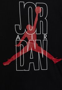 Schwarzes T-Shirt mit einer großen roten Silhouette einer springenden Figur und fettem weißem Text mit den Worten "JORDAN" und "AIR" in moderner Schriftart.