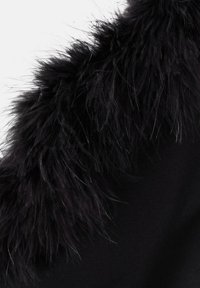 Sort beklædning med en fremtrædende pelsagtig tekstur langs halsudskæringen, med et blødt, luftigt udseende der kontrasterer mod en glat stofbund.