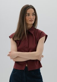 Burgundowa koszula z krótkim rękawem i wyłogami, o prostym kroju, wykonana z gładkiego materiału, w połączeniu z ciemnoniebieskimi spodniami z wysokim stanem.