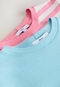 Deux T-shirts à manches courtes : l'un uni bleu clair, l'autre rayé rose et blanc. Chacun présente un col côtelé et une étiquette de marque.