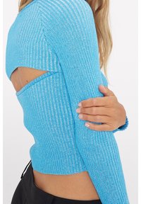 Maglione a coste di colore azzurro chiaro con aperture sui lati e maniche lunghe. Il materiale presenta una leggera lucentezza e una texture.