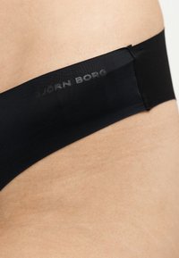 Ceinture élastique noire sur la peau avec l'inscription « BJÖRN BORG » imprimée en lettres gris foncé discrètes.