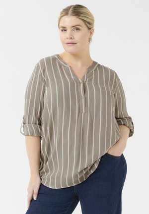 Blouse légère taupe avec des rayures verticales, manches retroussées, patte de boutonnage et coupe amples. Portée avec un pantalon en denim foncé.