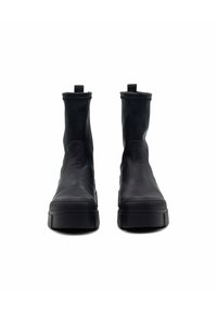 Bottines noires avec une tige en cuir lisse, des panneaux latéraux élastiques et une semelle épaisse. Caractéristiques d'une languette pour un enfilage facile.