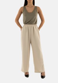 Haut en bronze à décolleté en V, associé à un pantalon ample couleur crème et des escarpins noirs, formant une tenue décontractée.