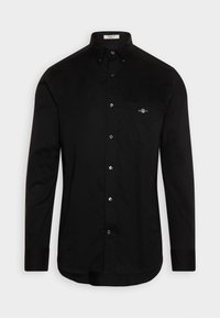 Chemise noire à manches longues boutonnée avec col et poche avant comportant un petit logo brodé sur la poitrine.