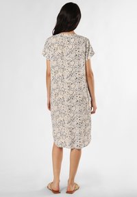 Kurzes, knielanges Kleid in Hellbeige mit floralem blauen Muster. Weiche Stoffqualität, lockerer Sitz und abgerundeter Saum. Kombiniert mit flachen Sandalen.