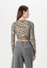 Long-sleeve, cropped top in beige with black leopard print; smooth texture. Paired with high-waisted, gray wide-leg jeans with back pockets.