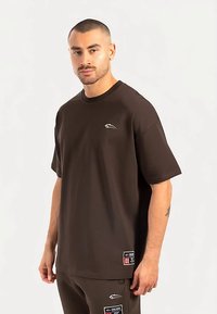 Braunes kurzärmeliges Hemd aus weichem Material mit Rundhalsausschnitt, versehen mit einem kleinen weißen Logo auf der Brust und einem Etikett mit der Nummer "01".