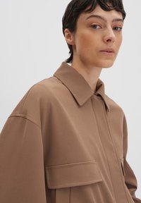 Bruine overhemdbloes met kraag, gemaakt van een gestructureerde stof, met een relaxte pasvorm en twee platte borstzakken.