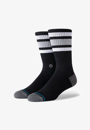 Schwarze Socken mit horizontalen Streifen in Weiß und Grau oben. Verstärkte graue Ferse und Zehen, mit einem kleinen Logo in der Nähe des Knöchels. Glatte Textur.