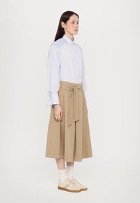 Cămașă în dungi albă și albastră cu mâneci lungi, fustă înfășurată khaki și adidași ușori. Material texturat cu un finisaj moale și detaliu cu fundiță.