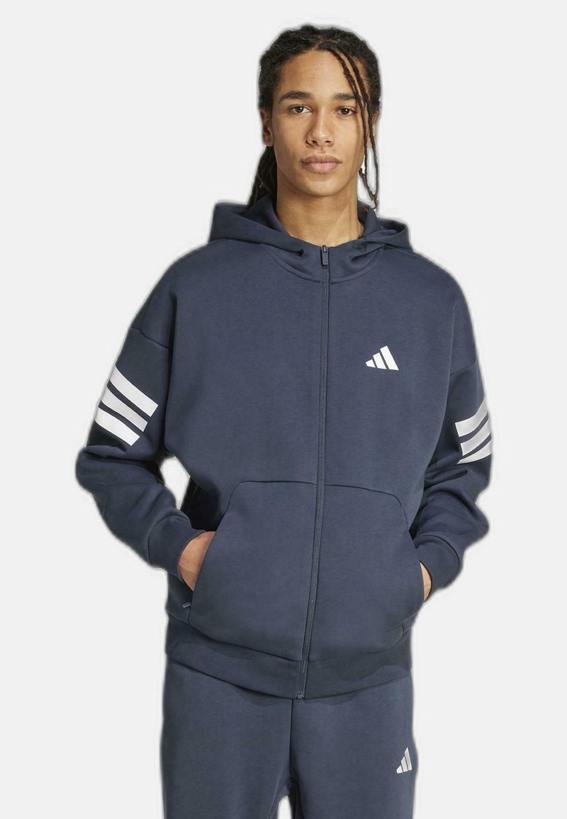 Navy zip-up hoodie with white Adidas logo on chest and three horizontal stripes on sleeves. Made from soft, textured fabric with a relaxed fit.
