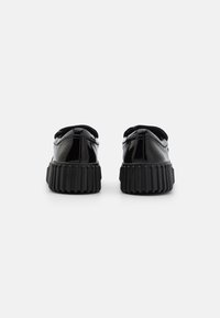 Chaussures en cuir verni noir avec un bout rond, un talon arrondi et une semelle striée, présentant un dessus lisse et des coutures décoratives au niveau du talon.