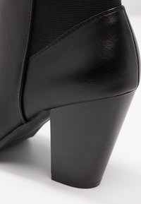 Sort læder ankelstøvle med en chunky blokhælhæl og elastisk sidepanel, fotograferet mod en hvid baggrund.