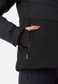 Veste imperméable noire avec une poche zippée et des poignets élastiques. Le tissu a une texture lisse avec un léger éclat.