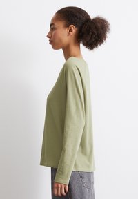 Langermet genser med rund hals i lysegrønn bomull. Har en avslappet passform, sidesømmer og et enkelt design, brukt med grå jeans.