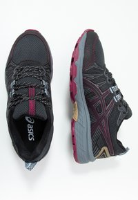 Chaussures de sport noires avec une tige en mesh, des accents violets et gris, une semelle texturée et des lacets réfléchissants, équipées d'un col et d'une languette rembourrés.