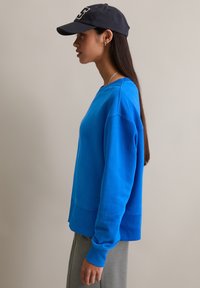 Jasnoniebieska bluza z okrągłym dekoltem, ściągaczami na rękawach i dole. W zestawie z szarym dołem i granatową czapką z daszkiem z białym logo.