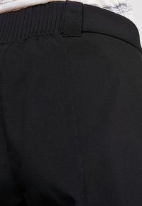 Gros plan sur un pantalon de sport noir doté d'une ceinture côtelée, d'une texture lisse et de coutures verticales, conçu pour le confort et la mobilité.