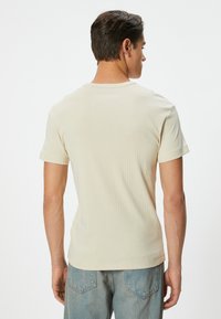 Beige ribbet kortærmet t-shirt med rund hals. Stoffet har en blød tekstur og vises sammen med lyseblå jeans.