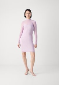 Light pink, fitted long-sleeve dress with a soft, sheer texture and subtle pattern, paired with strappy high heels.