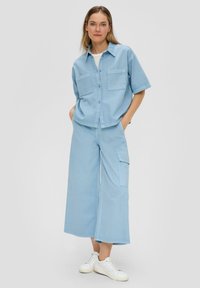 Light blue denim shirt with two chest pockets, paired with wide-leg blue jeans featuring a side cargo pocket. White sneakers complete the outfit.