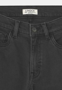 Jeans in denim nero con un design classico, dotati di chiusura con bottone, cinque tasche e un'etichetta che indica taglia e origine.