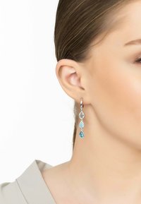Ezüst fülbevalók három csepp alakú kék és aqua kövekkel, gyűrűről lógva, rétegzett kialakítással és sima textúrával.